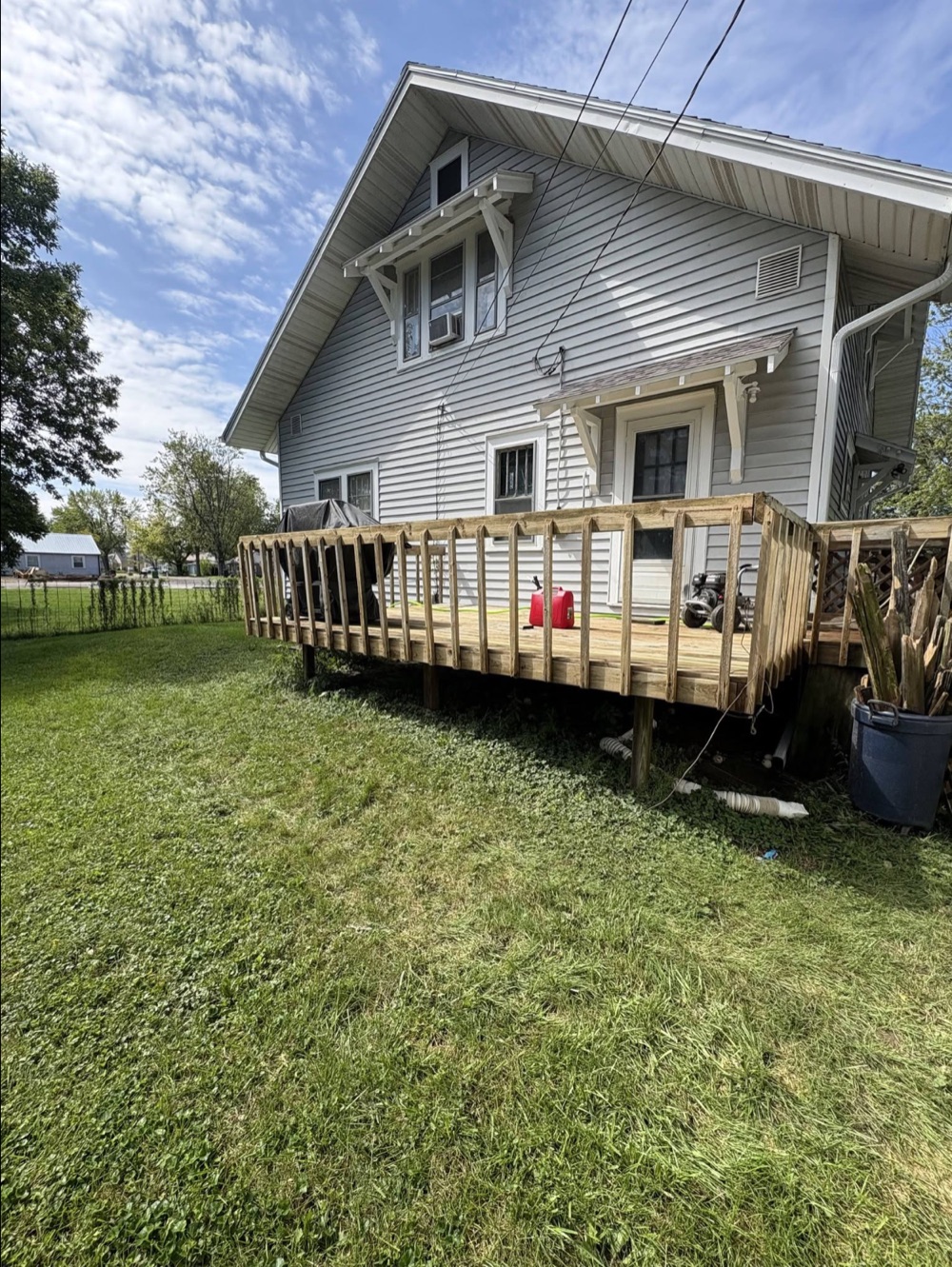 After photo of the same gray-sided house exterior and wood deck beneath a blue sky