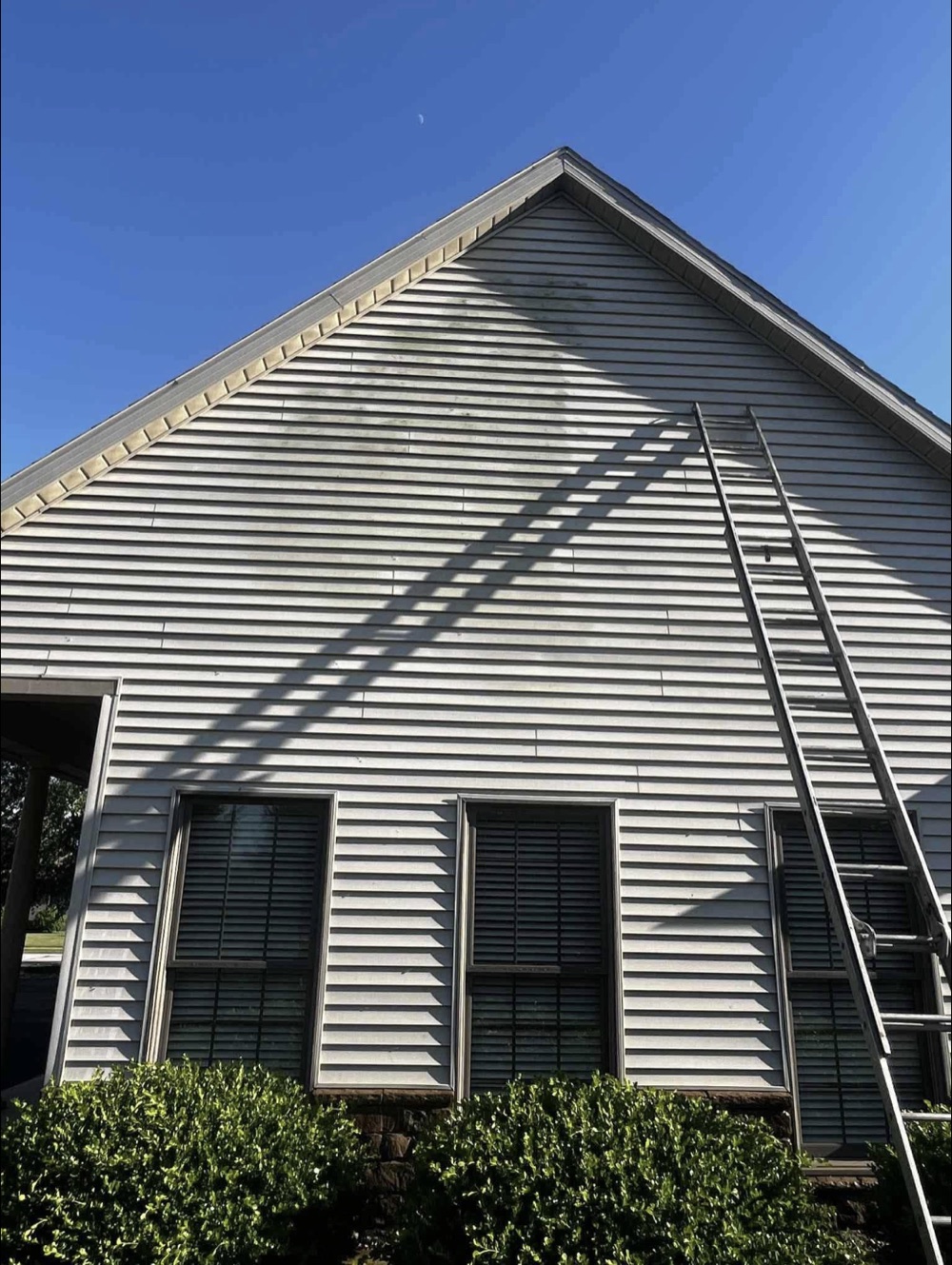 Ladder leaned against a house exterior beneath a clear blue sky