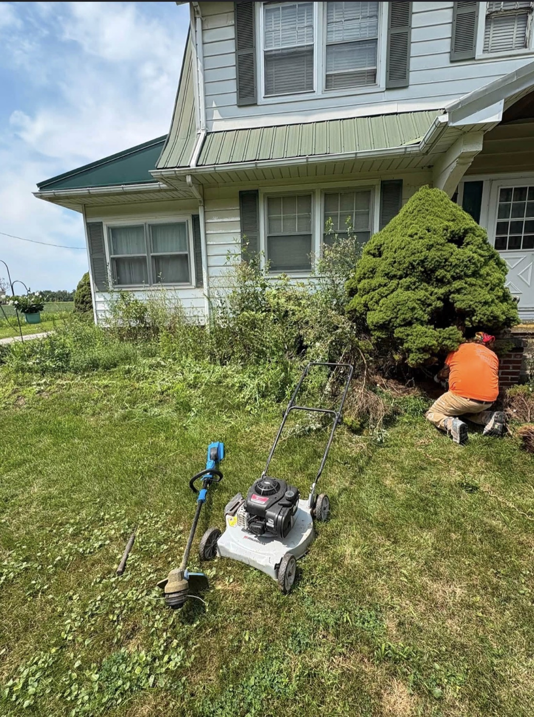 Outdoor cleanup work in progress at a home, with a mower and trimmer in the foreground